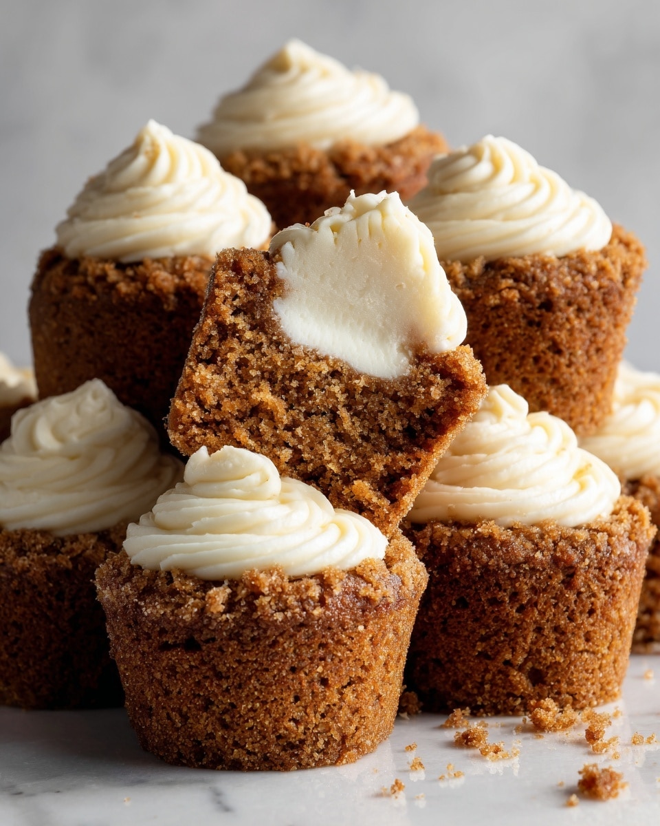 A close-up image of several small brown muffins with a crumbly, slightly rough texture, each topped with a swirl of creamy white frosting. Two muffins are cut in half, revealing a thick, smooth white cream filling inside. The muffins are piled together against a white marbled background, showing a contrast between the warm brown of the muffins and the bright white of the filling and frosting. The frosting looks soft and slightly glossy, sitting neatly on top of each muffin, while the crumb topping adds a textured look to the surface. photo taken with an iphone --ar 4:5 --v 7