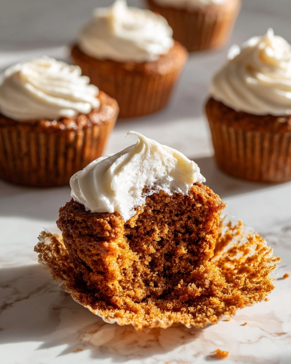 A close-up image of a partly eaten muffin with a rough, crumbly brown texture showing a moist inside. On top of the muffin is a large dollop of smooth, creamy white frosting with a slightly whipped texture. In the background, there are three more muffins, each topped with the same white frosting, all placed on a white marbled surface with soft shadows and natural light highlighting the textures. photo taken with an iphone --ar 4:5 --v 7
