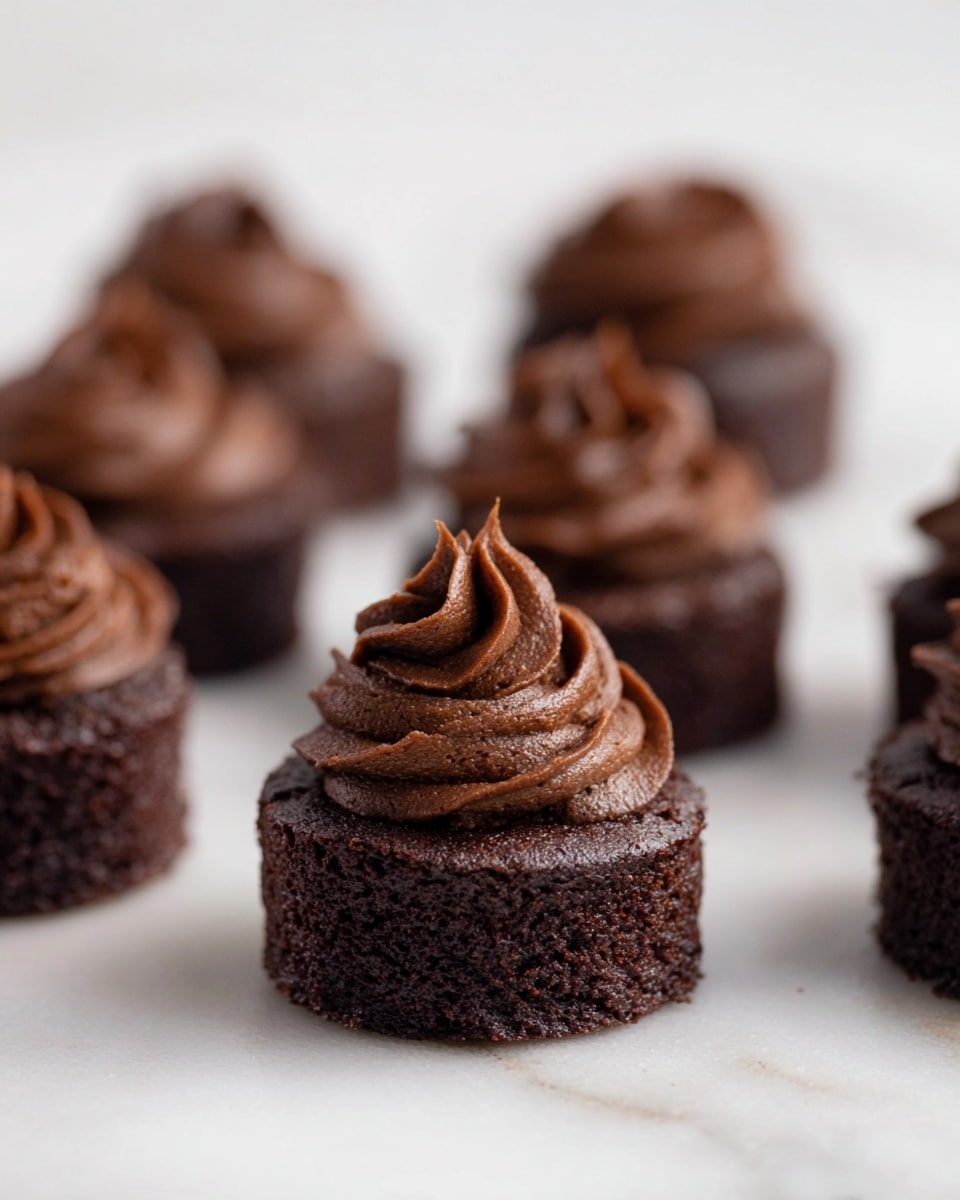 The image shows several small, round chocolate cakes placed on a white marbled surface. Each cake has two layers: a dense, dark brown cake base with a slightly cracked texture, and a thick, swirled layer of rich chocolate frosting on top. The frosting is darker and smoother, piped high in a spiral shape with detailed ridges. The cakes are arranged with some in sharp focus in the center and others softly blurred in the background and foreground. photo taken with an iphone --ar 4:5 --v 7