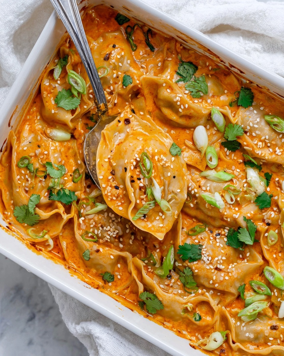 The image shows a white baking dish filled with several layers of dumplings covered in a thick orange sauce. The dumplings have a soft, slightly browned texture and are topped with small green onion pieces and white sesame seeds scattered evenly across the surface. Fresh cilantro leaves add a bright green touch on top. A silver spoon is lifting a few dumplings, showing their folded shape and the creamy orange sauce coating them. The dish is placed on a white marbled surface with a white cloth partially visible to the side. Photo taken with an iphone --ar 4:5 --v 7