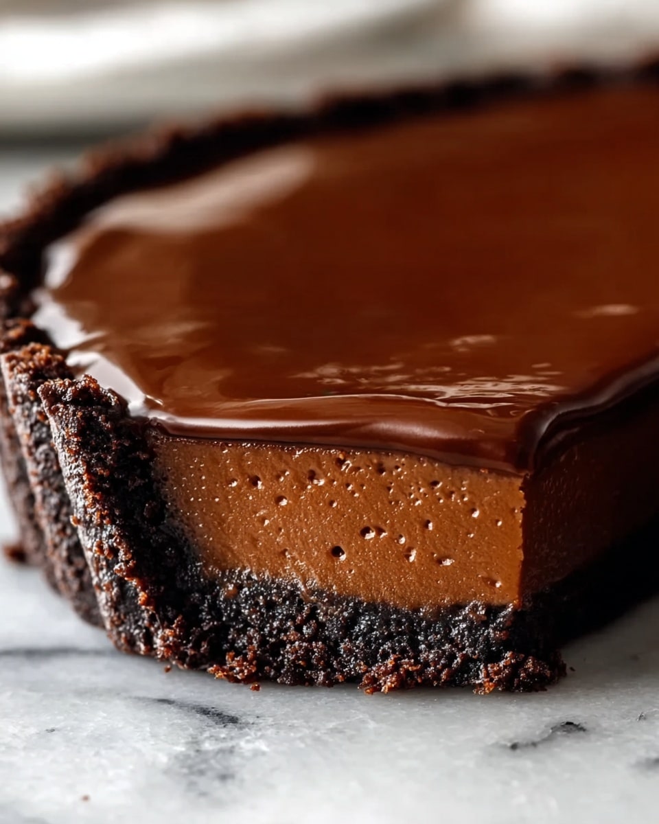 A close-up of a chocolate tart with three visible layers sitting on a white marbled texture. The bottom layer is a dark, crumbly chocolate crust with a rough texture. Above that is a thick, smooth milk chocolate filling, slightly glossy with tiny air bubbles. The top layer is a shiny, dark chocolate glaze that looks smooth and reflective, slightly dripping over the edge of the tart shell. The crust edge is crimped, adding texture and shape to the tart's border. photo taken with an iphone --ar 4:5 --v 7