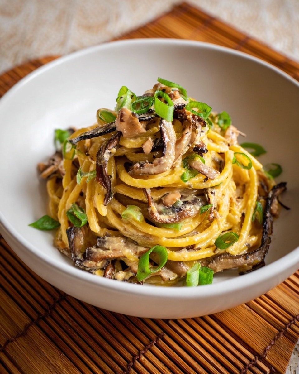 A white bowl holds a serving of creamy pasta twisted into a small mound. The pasta is yellow with a smooth, glossy texture coated in a light brown cream sauce. Thin, wavy dark brown mushroom slices are mixed throughout, adding a slight crisp look to the dish. Bright green onion rings are scattered on top and around the pasta, adding fresh color contrast. The bowl sits on a wooden board with a bamboo mat underneath. photo taken with an iphone --ar 4:5 --v 7