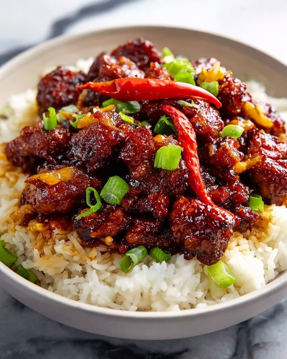 A white bowl filled with a base layer of fluffy white rice with a slightly grainy texture, topped by a thick, glossy layer of dark reddish-brown glazed meat pieces that look crispy yet coated in a sticky sauce, scattered with bright green chopped scallions and a few whole red chili peppers for color contrast. The bowl is placed on a white marbled surface. photo taken with an iphone --ar 4:5 --v 7