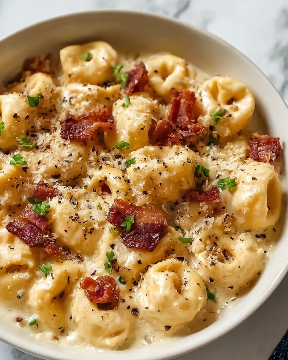 A close-up view of a white bowl filled with creamy tortellini pasta. The tortellini are coated in a smooth, pale yellow cheese sauce, creating a rich and velvety texture. On top, there are small, crispy red bacon pieces scattered evenly, along with finely chopped green herbs for a touch of freshness. The dish is sprinkled with grated parmesan cheese and black pepper, adding a grainy texture and specks of black. The background features a white marbled surface, enhancing the creamy colors of the pasta. Photo taken with an iphone --ar 4:5 --v 7