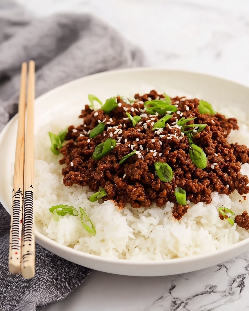 A white shallow bowl holds a base layer of fluffy white rice with distinct grains. On top is a thick layer of cooked ground beef, rich brown in color with a slightly crumbly texture. Scattered across the beef are small white sesame seeds and chopped green onions, adding pops of white and fresh green colors. A pair of light wooden chopsticks with a black and white patterned tip rests on the bowl’s edge. The bowl is placed on a white marbled surface with a soft gray cloth blurred in the background. photo taken with an iphone --ar 4:5 --v 7