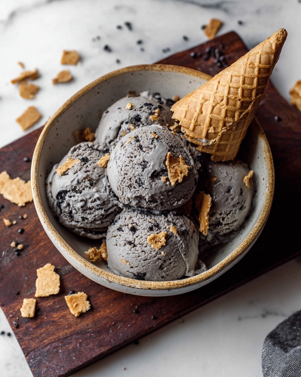A bowl with five scoops of grayish-black ice cream, mixed with small black seeds or bits, topped with scattered pieces of light brown broken waffle cone. A broken waffle cone lies on the side inside the bowl. The bowl is placed on a dark wooden board, set on a white marbled surface. Photo taken with an iphone --ar 4:5 --v 7